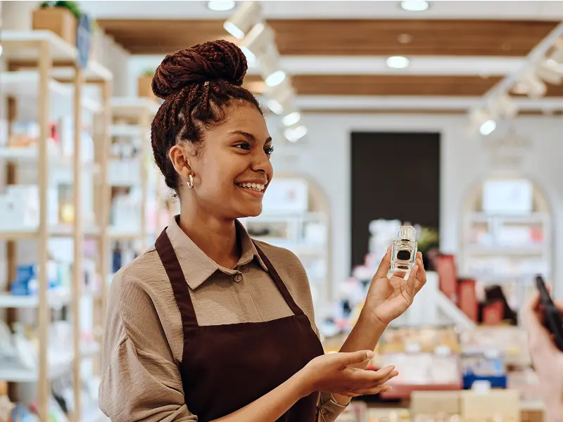 Une vendeuse souriante tenant un flacon de parfum