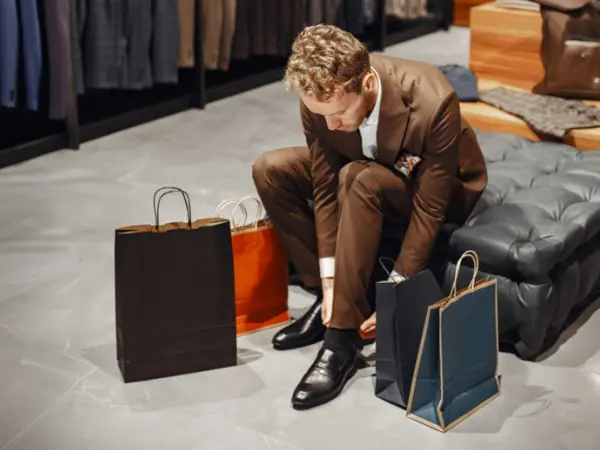 Un homme en train d'essayer des chaussures dans un magasin, entouré de sacs de courses