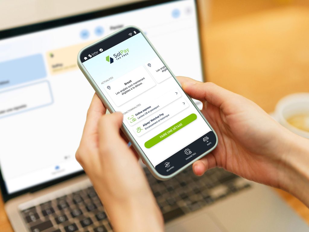 Zoom sur le téléphone d'une personne qui utilise le logiciel solpay devant un ordinateur